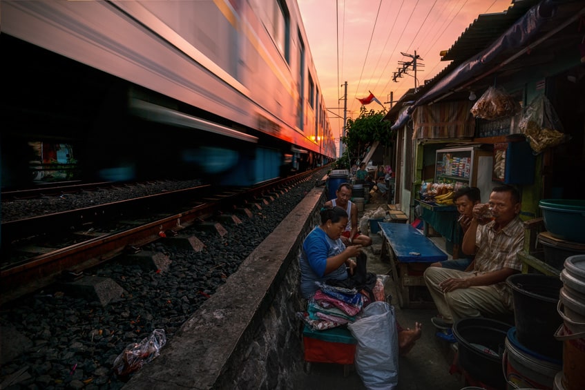 people sitting at their slum houses while a train rushes close by